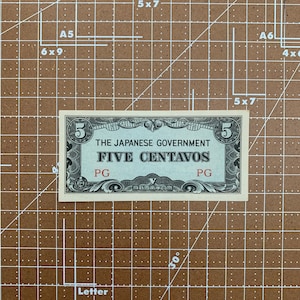 May include: A vintage five centavo banknote issued by the Japanese Government. The note is printed on paper with a light brown background and features a black and white design. The note has the text "THE JAPANESE GOVERNMENT FIVE CENTAVOS" printed in black.