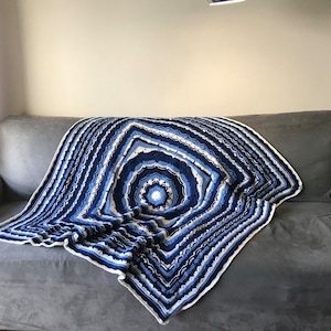May include: A blue and white crocheted blanket with a circular pattern in the centre, draped over a grey sofa.