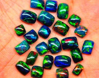 Puede incluir: Una colección de piedras preciosas de ópalo negro pulidas con vibrantes destellos verdes, azules y rojos. Los ópalos son rectangulares y cuadrados, mostrando su juego de colores único. Ideales para la creación de joyas.