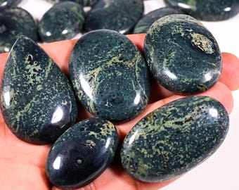 May include: A collection of polished, oval-shaped gemstones in shades of dark teal and green. The stones have a marbled appearance with lighter green and tan veining. Some stones are teardrop-shaped. The gemstones are held in a hand.