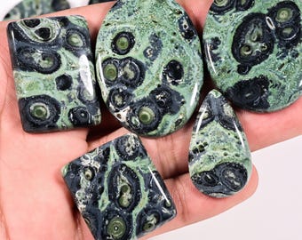 May include: A collection of polished gemstones in various shapes, including oval, rectangular, and teardrop. The stones feature a unique pattern of green and black swirls and spots, with a glossy finish. These stones are ideal for jewelry making.