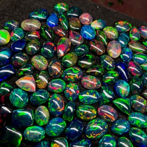 May include: A collection of black opal gemstones with iridescent green, blue, and red colours. The opals are displayed on a black surface.