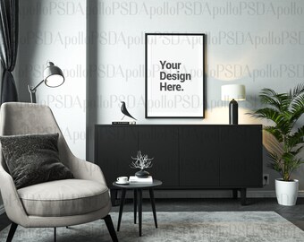 May include: A black framed picture with the text "Your Design Here." hanging on a wall above a black cabinet. A gray armchair with a black pillow sits in front of the cabinet. A small table with a cup and saucer sits in front of the chair. A potted plant sits on the floor next to the cabinet.