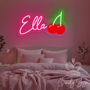 May include: Pink neon sign with the name "Ella" and a cherry with a green stem. The sign is hanging on a pink wall above a bed with pink bedding.