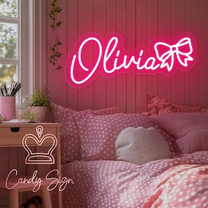 May include: Pink neon sign with the name "Olivia" and a bow. The sign is mounted on a pink wall in a bedroom setting.