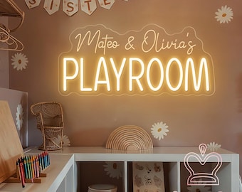 May include: A custom neon sign mounted on a wall, glowing with warm yellow light and displaying the text Mateo & Olivia's PLAYROOM in a script and sans-serif font combination. The sign is mounted on a wall decorated with white daisy decals.