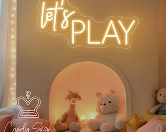 May include: A neon sign that reads "let's PLAY" in a playful font. Below the sign is a decorative alcove with stuffed animals and a toy train. The sign is from Candy Sign.