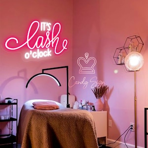 Könnte beinhalten: Rosafarbenes Neon-Schild mit dem Text "It's lash o'clock" in einer kursiven Schriftart. Unter dem Schild befindet sich eine Kronengrafik mit dem Text "Candy Sign".