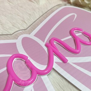 May include: A pink and white decorative sign with the word "one" in a cursive font. The sign has a bow-shaped design and the text "Candy Six" is visible.