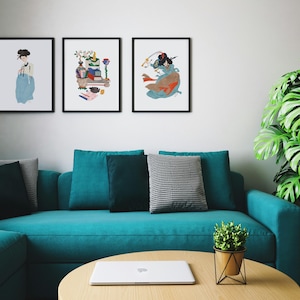 May include: Three framed art prints with black frames hang above a teal sofa. The prints feature illustrations of Asian women in traditional clothing. A round wooden coffee table with a laptop and a small potted plant complete the scene.