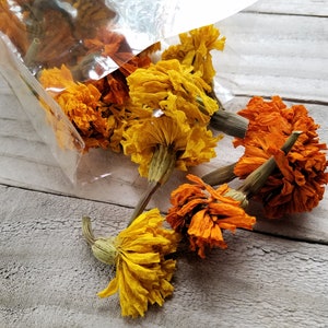 Puede incluir: Flores de cal&eacute;ndula secas en tonos naranja y amarillo, que se derraman de una bolsa de pl&aacute;stico transparente sobre una superficie de madera clara.