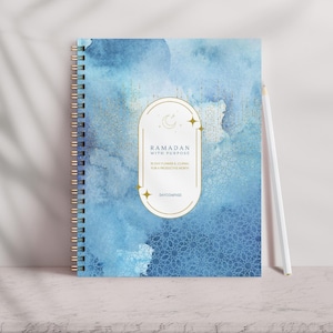 May include: A blue and gold spiral bound journal with the text "Ramadan with Purpose" and a crescent moon and stars design. The journal is on a white surface.