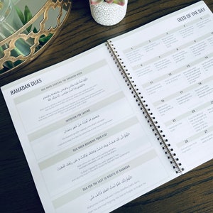 May include: A Ramadan planner with a beige cover and gold spiral binding. The planner includes a section for daily deeds, duas for different occasions, and a section for the last 10 nights of Ramadan. The text is in Arabic and English.