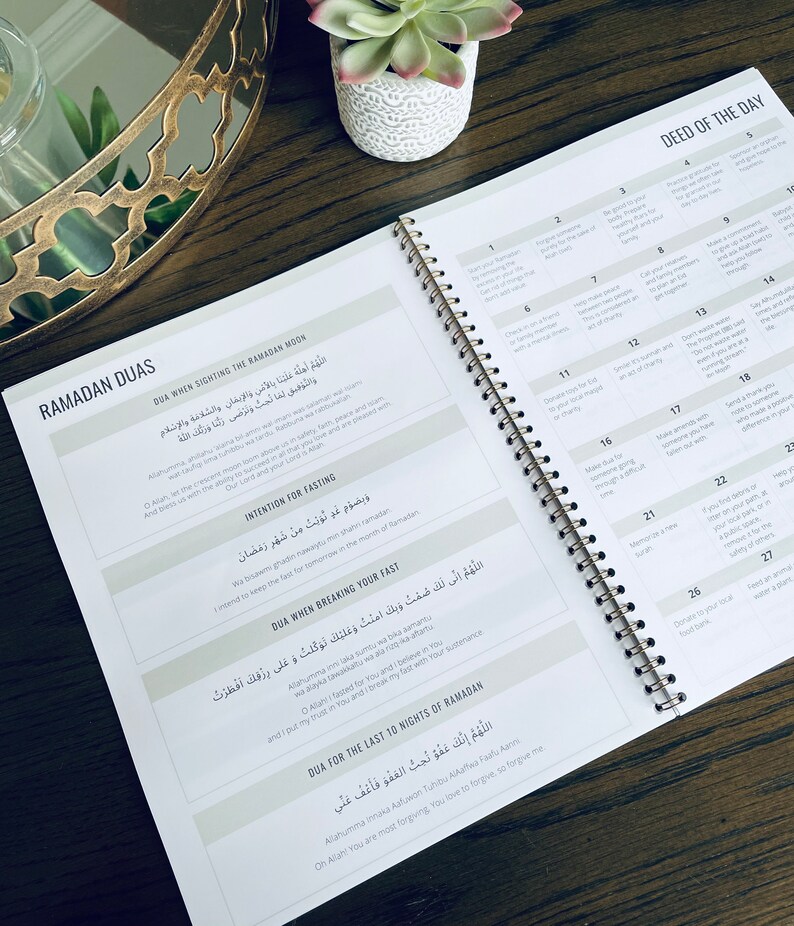 May include: A Ramadan planner with a beige cover and gold spiral binding. The planner includes a section for daily deeds, duas for different occasions, and a section for the last 10 nights of Ramadan. The text is in Arabic and English.