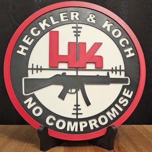 May include: A round, multi-layered sign with the text "HECKLER & KOCH" and "NO COMPROMISE". The sign features a red border, black and white accents, and a red "HK" logo. A black firearm is in the center.