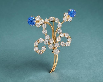 Broche vintage con diseño floral de los años 50 y 60, con diamantes de imitación en tono dorado y zafiro azul. Joyería de fantasía. Broche llamativo de mediados de siglo.