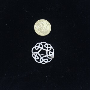 May include: A silver Celtic knot brooch with a pin closure. The brooch is about the size of a US quarter.