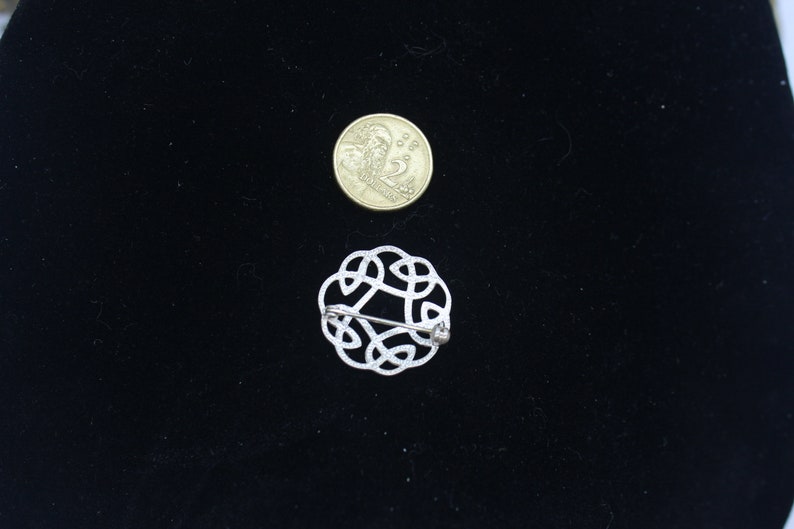 May include: A silver Celtic knot brooch with a pin closure. The brooch is about the size of a US quarter.