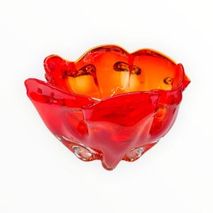 May include: A red and orange glass bowl with a wavy, organic shape. The bowl is made of hand-blown glass and has a unique, modern design.