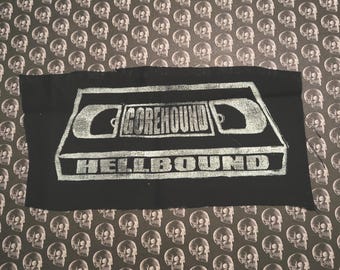 Peut inclure: Patch en tissu noir avec un graphique blanc d'une cassette VHS avec le texte "Gorehound Hellbound" imprimé dessus.