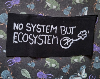 May include: Black fabric patch with white text that reads "No System But Ecosystem" and a white drawing of a flower with a stem and a circle at the end of the stem.
