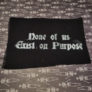 May include: Black fabric patch with white text that reads "None of us exist on purpose".
