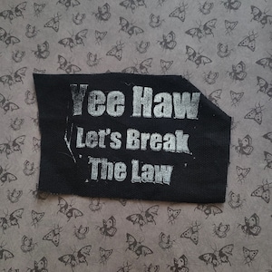 May include: Black fabric patch with white text that reads "Yee Haw Let's Break The Law".