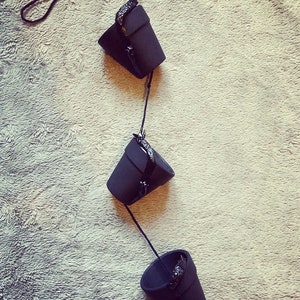 May include: Three black hanging planters with a black cord connecting them. The planters are made of a textured material and have a slightly rounded shape.