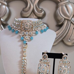 May include: An elegant jewelry set featuring a gold-toned choker necklace, a headpiece, and matching earrings. The set is adorned with light blue gemstones and small white pearls, creating a sophisticated and eye-catching design.
