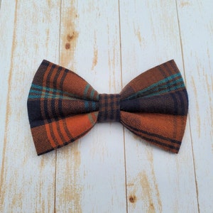 A navy blue, orange, and turquoise plaid flannel bow tie sitting on a white-washed wood surface.
