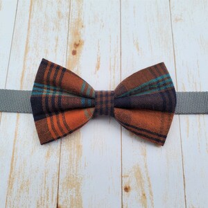 May include: A plaid bow tie with orange, blue, and black colors. The bow tie is attached to a gray strap.