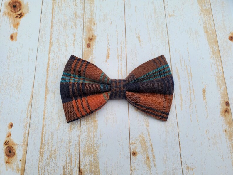 A navy blue, orange, and turquoise plaid flannel bow tie sitting on a white-washed wood surface.