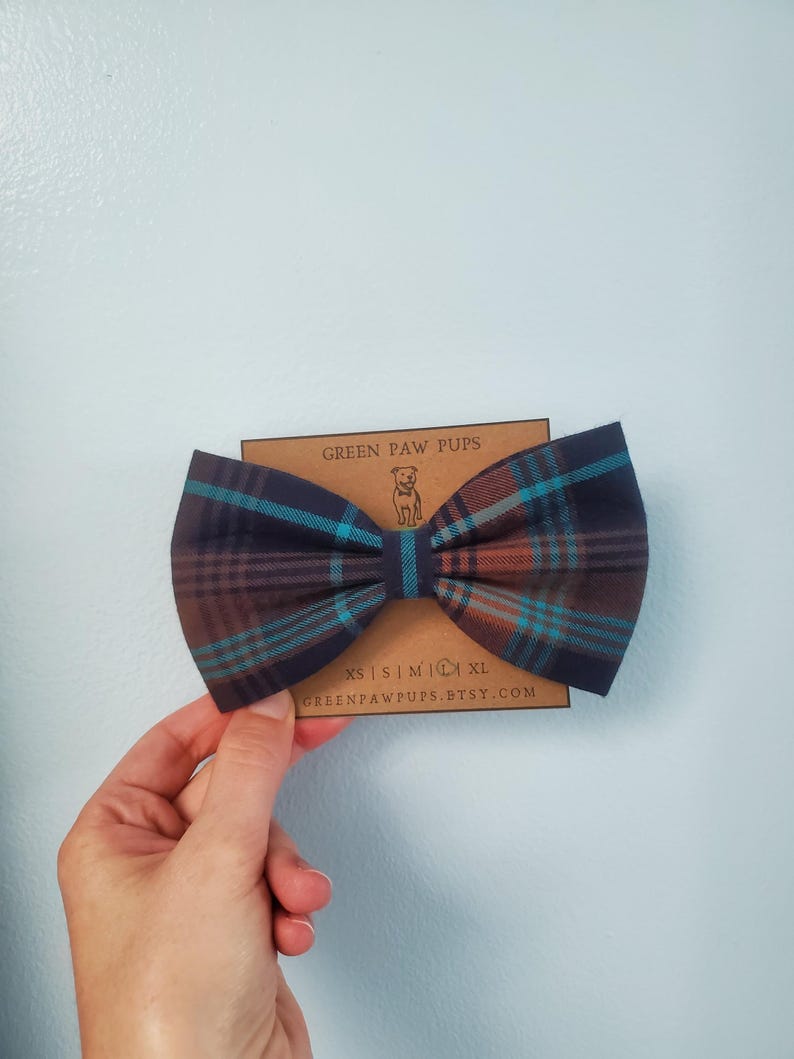 May include: A brown, blue, and orange plaid bow tie for a dog. The bow tie is on a brown card with the text "GREEN PAW PUPS" and "GREENPAWPUPS.ETSY.COM".