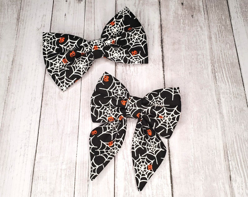 May include: Two black fabric bow ties with a white spiderweb and orange pumpkin pattern.