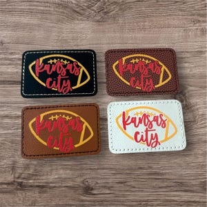 May include: Four rectangular patches with a football design and the words "Kansas City". The patches are black, brown, and white, with the footballs in yellow and the text in red. The patches are stitched with white thread.