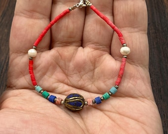May include: A handmade bracelet featuring a central blue bead with gold accents, surrounded by colorful beads in red, blue, green, and white. The bracelet is strung on a red cord and has a silver clasp. A unique piece of jewelry.