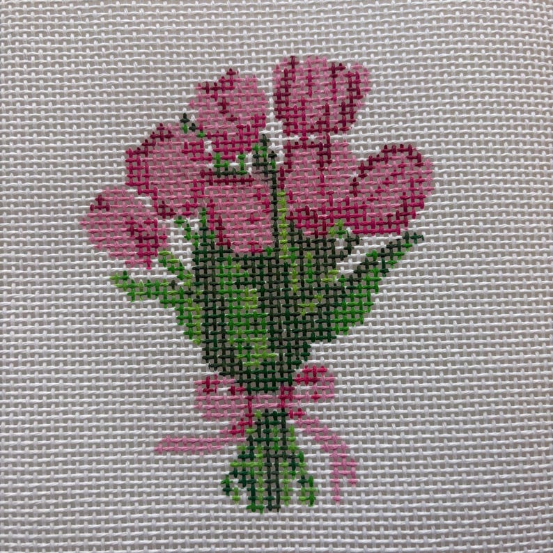 May include: A cross-stitch design of a bouquet of pink tulips tied with a pink ribbon. The tulips have varying shades of pink, and the leaves are green. The background is a light gray fabric.