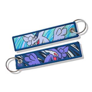 May include: Two blue and white keychains with a blue and white swirl pattern. The keychains feature a cartoon image of a white and purple creature with wings.