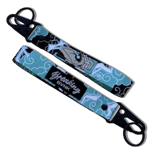 May include: A black and blue key chain with a white cloud pattern and the text "Breaking BVNK". The key chain has a black metal clasp and a black metal ring.