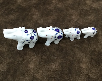 May include: Four white marble elephants of varying sizes, each decorated with blue and red floral patterns. The elephants are arranged in a line from largest to smallest.