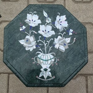 May include: Octagonal green marble table top with a floral design inlaid with white and blue mother of pearl. The design features a vase with flowers and leaves.