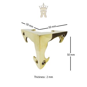 Puede incluir: Un soporte de esquina de color lat&oacute;n con un dise&ntilde;o decorativo. El soporte mide 5 cm por cada lado y 5 cm de alto, con un grosor de 2 mm. Cuenta con tres recortes curvos y tres orificios para tornillos. Tambi&eacute;n incluye el texto "Thickness: 2 mm".