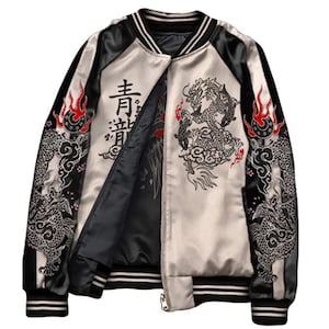 Puede incluir: Chaqueta bomber de satén con cuerpo color crema y mangas negras. La chaqueta presenta intrincados bordados de dragones en negro y rojo, con caracteres japoneses en la parte delantera. Los puños y el cuello tienen rayas blancas y negras.