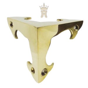 May include: A gold-colored, corner bracket with a decorative design. The bracket has a triangular shape with curved edges and three holes for mounting. The bracket is made of metal and has a shiny finish.