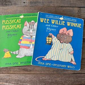 Può includere: Sono esposti due libri per bambini vintage, "Pussycat Pussycat and Other Rhymes" e "Wee Willie Winkie and Other Rhymes". I libri presentano illustrazioni colorate di un gatto e un topo. I titoli e i nomi degli autori sono visibili.