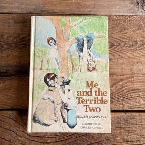 May include: A vintage children's book cover with a colorful illustration of two children and a dog. The title is "Me and the Terrible Two" by Ellen Conford, illustrated by Charles Carroll.