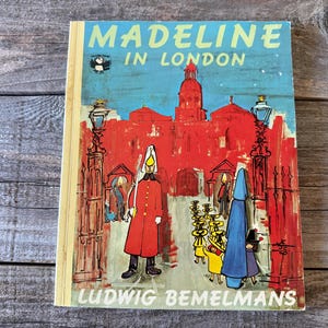 May include: Vintage children's book titled "Madeline in London" by Ludwig Bemelmans. The cover features a vibrant illustration of a London scene with red buildings, figures in red coats, and the title in blue and yellow.
