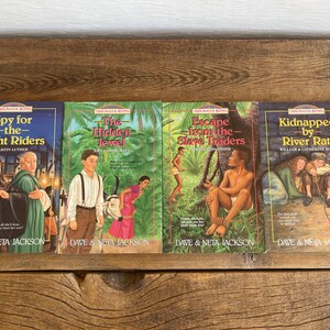 以下が含まれることがあります： 冒険と歴史小説に関連するカラフルな表紙とタイトルがついたペーパーバックの書籍が4冊あります。書籍のタイトルは「スパイ・フォー・ザ・ナイト・ライダーズ」、「ザ・ヒドゥン・ジュエル」、「エスケープ・フロム・ザ・スレイブ・トレーダーズ」、「キッドナップド・バイ・リバー・ラッツ」です。