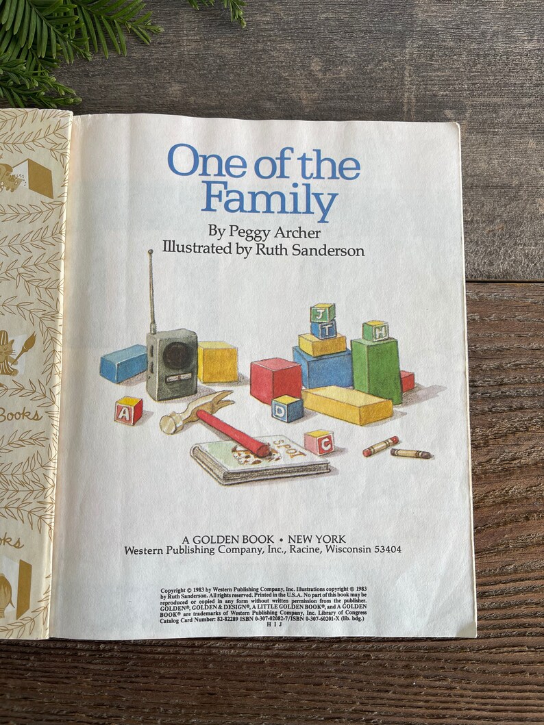 Pu&ograve; includere: Un libro vintage Golden Book intitolato "One of the Family" di Peggy Archer, illustrato da Ruth Sanderson. La copertina del libro presenta un'illustrazione colorata di un bambino che gioca con blocchi di legno e una radio giocattolo.