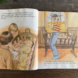 Pu&ograve; includere: Un'illustrazione di un libro per bambini che mostra un bambino in una culla con due fratelli maggiori. Il bambino sta guardando il fratello maggiore che tiene un libro. L'altro fratello &egrave; in piedi dietro la culla. Il testo sulla pagina dice: "Con il passare delle settimane, Melissa ha iniziato a rimanere sveglia un po' pi&ugrave; a lungo. Ora, quando Carrie le cantava, Melissa la fissava con occhi grandi e aperti e calciava con i piedi. E quando Craig ballava, lei seguiva i suoi movimenti con lo sguardo. Una volta, si &egrave; persino rotolata."